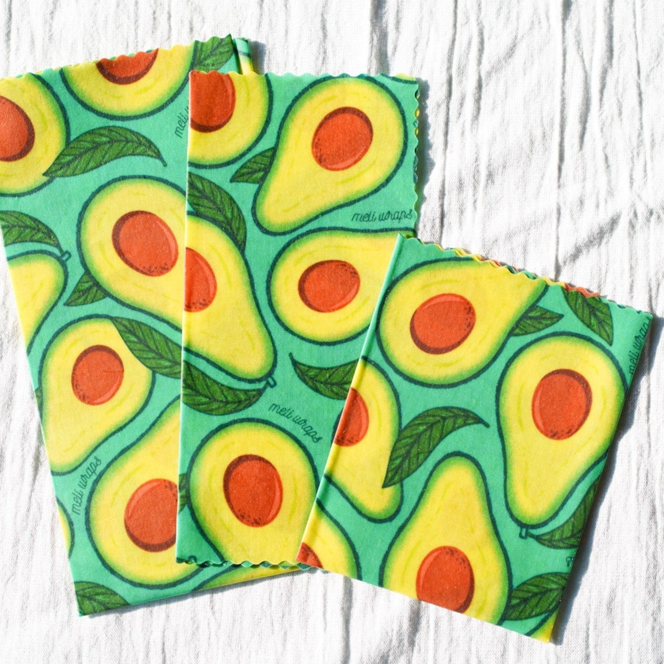 Two reusable shopping bags with avocado pattern on a light wooden surface