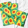 Two reusable shopping bags with avocado pattern on a light wooden surface