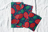 Two fabric swatches with a vibrant red and green pomegranate pattern on a blue background.