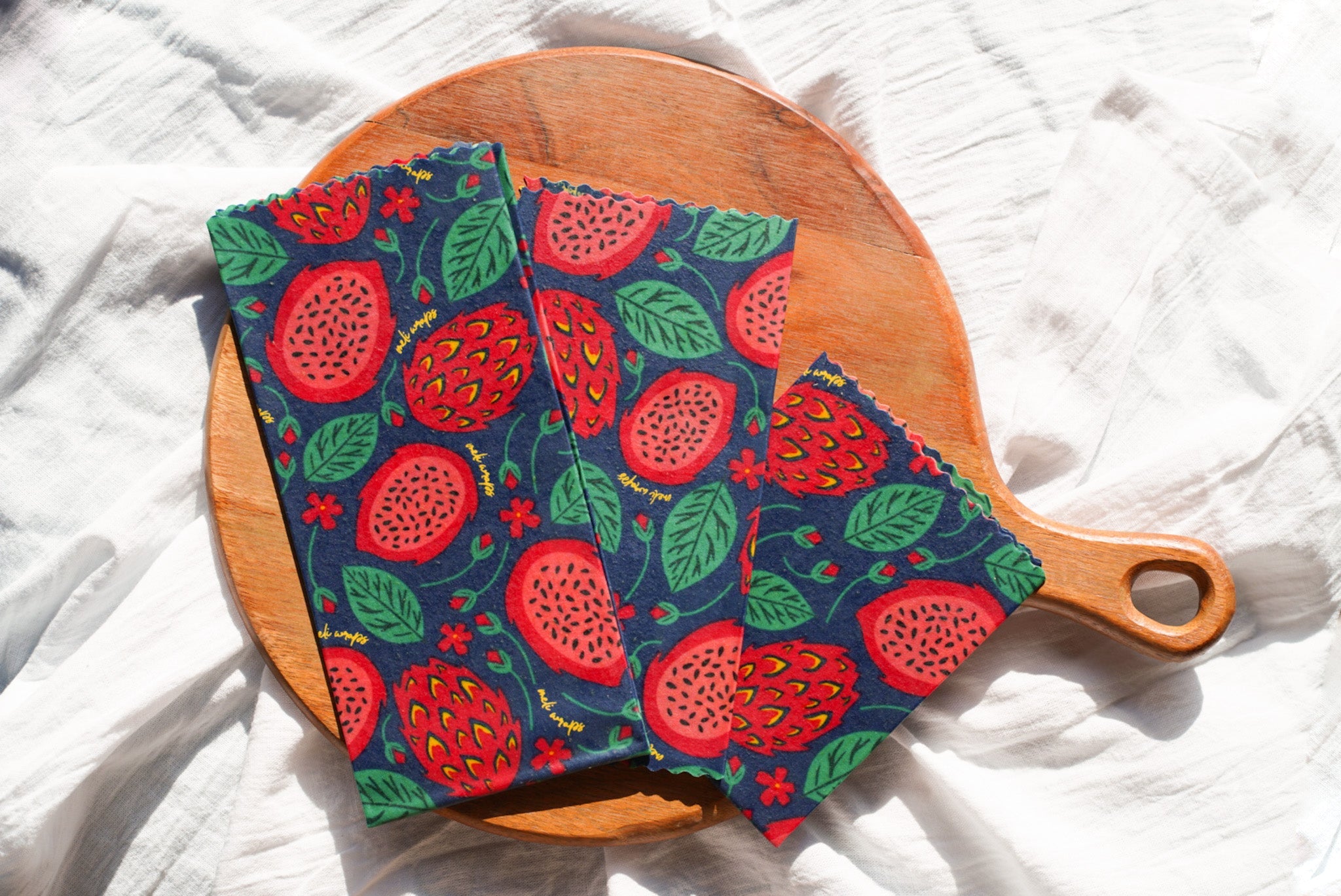 Two colorful fabric hot pads with a pomegranate pattern on a wooden cutting board.