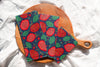 Two colorful fabric hot pads with a pomegranate pattern on a wooden cutting board.