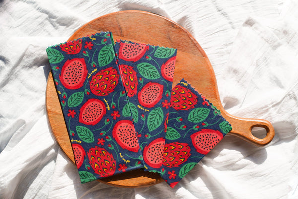 Two colorful fabric hot pads with a pomegranate pattern on a wooden cutting board.