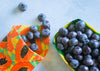 Blueberries on a colorful paper plate and in a green container on a light surface.