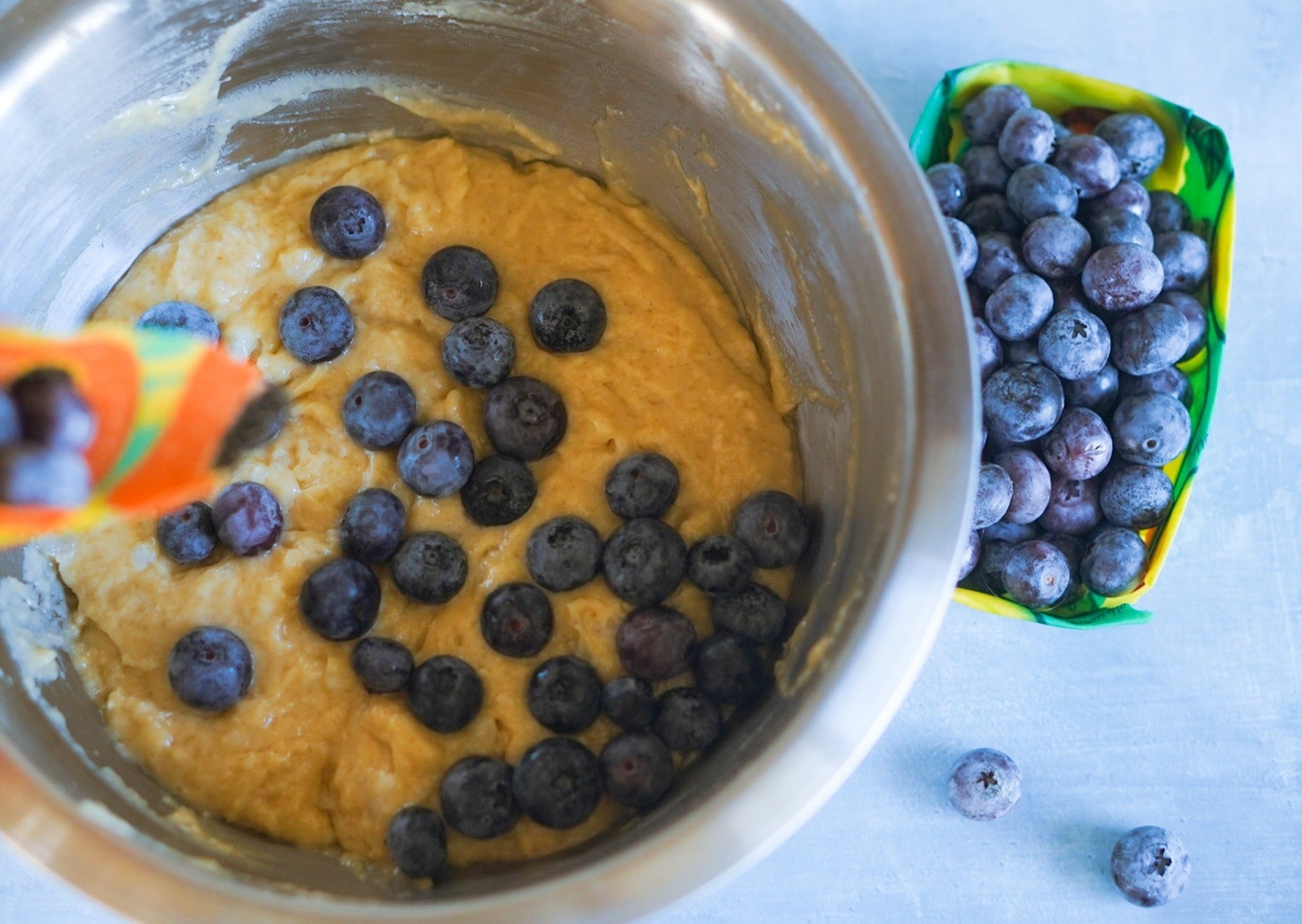 Bowl of blueberry muffin batter with blueberries being added