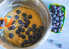 Bowl of blueberry muffin batter with blueberries being added