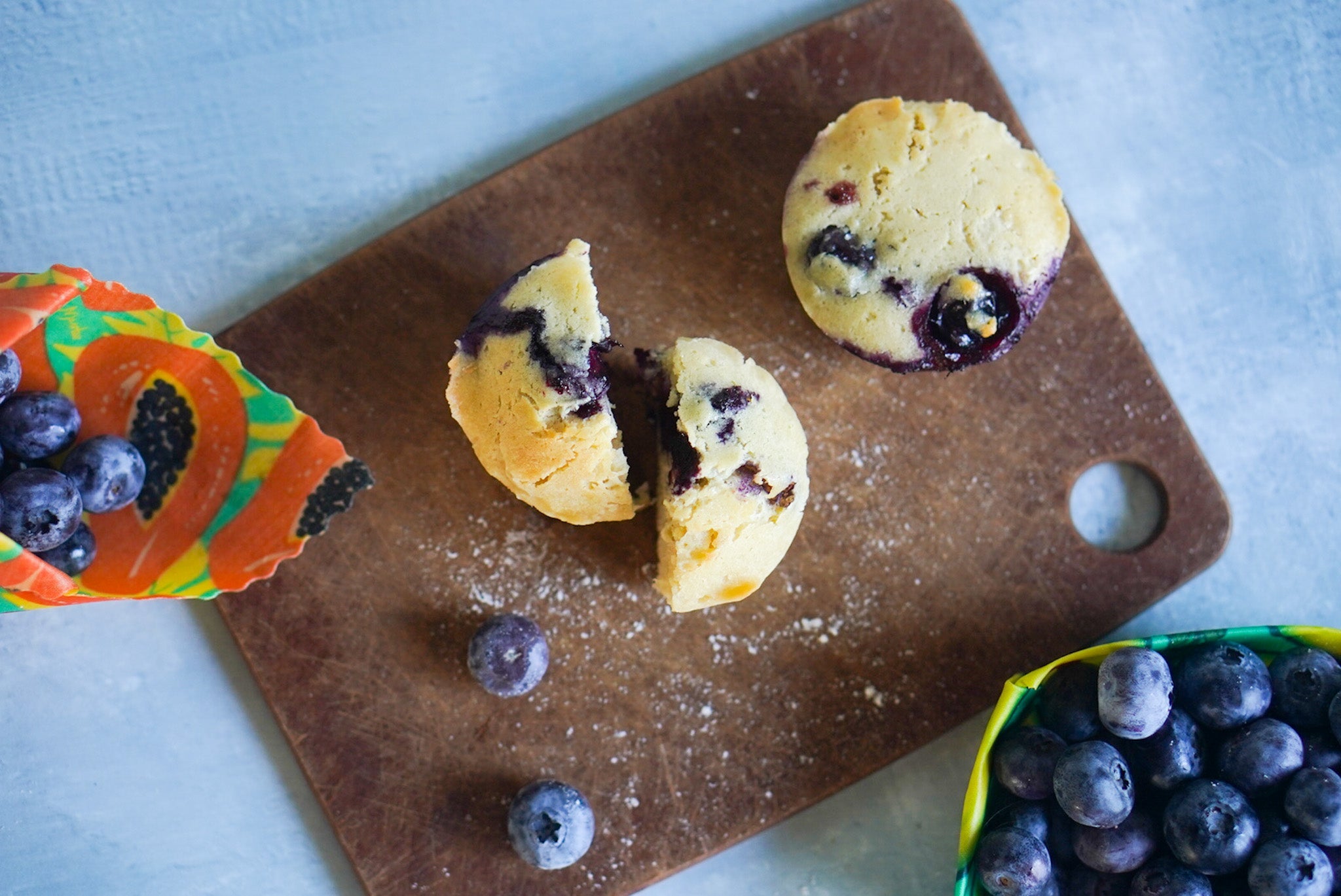 Blueberry muffin cut in half on a wooden cutting board with blueberries around.