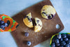 Blueberry muffin cut in half on a wooden cutting board with blueberries around.