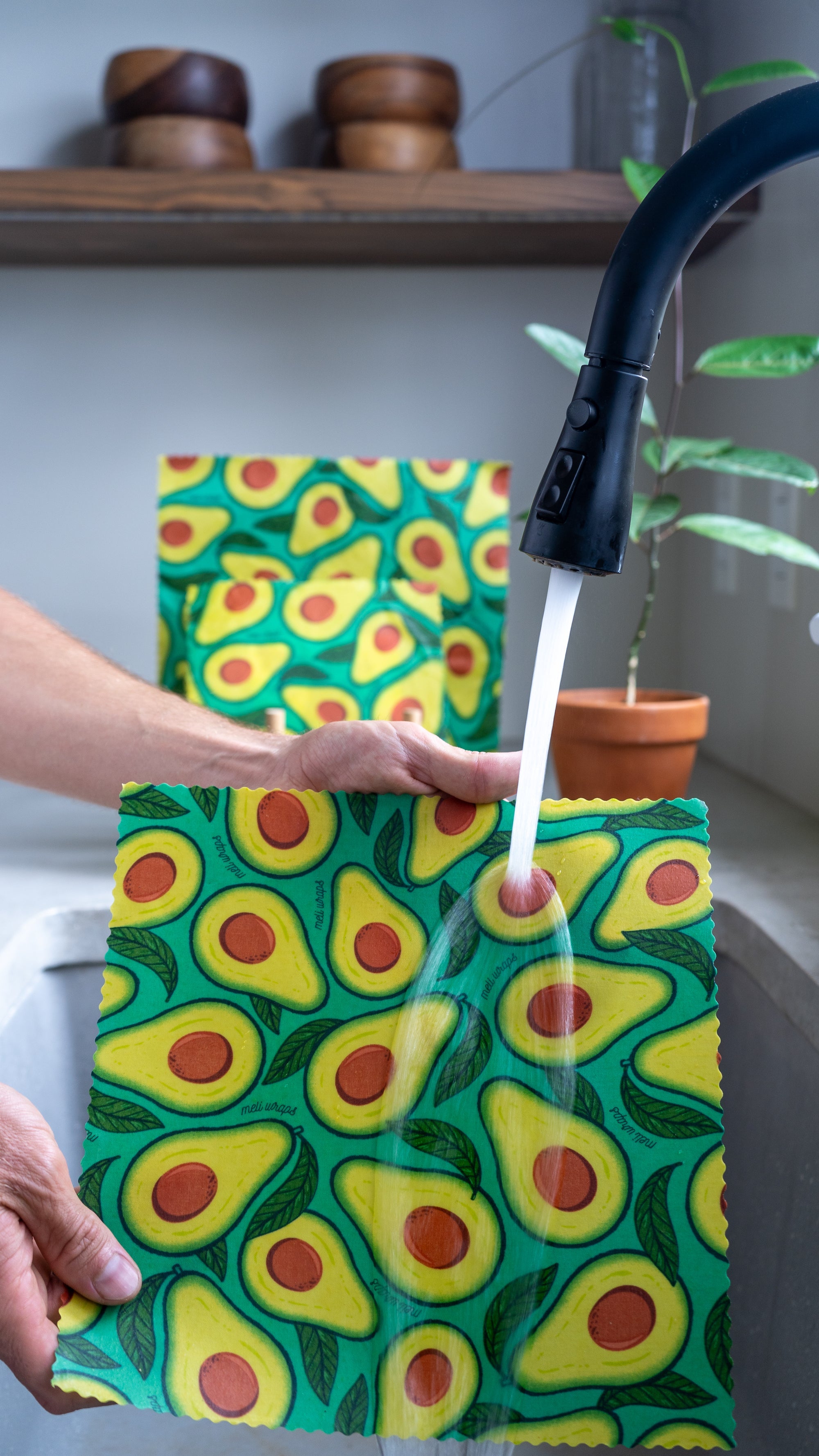 Avocado-patterned towel being rinsed under a faucet with a kitchen setting in the background.