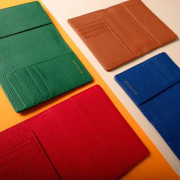 Four colorful leather card holders (green, brown, red, blue) on a beige background.