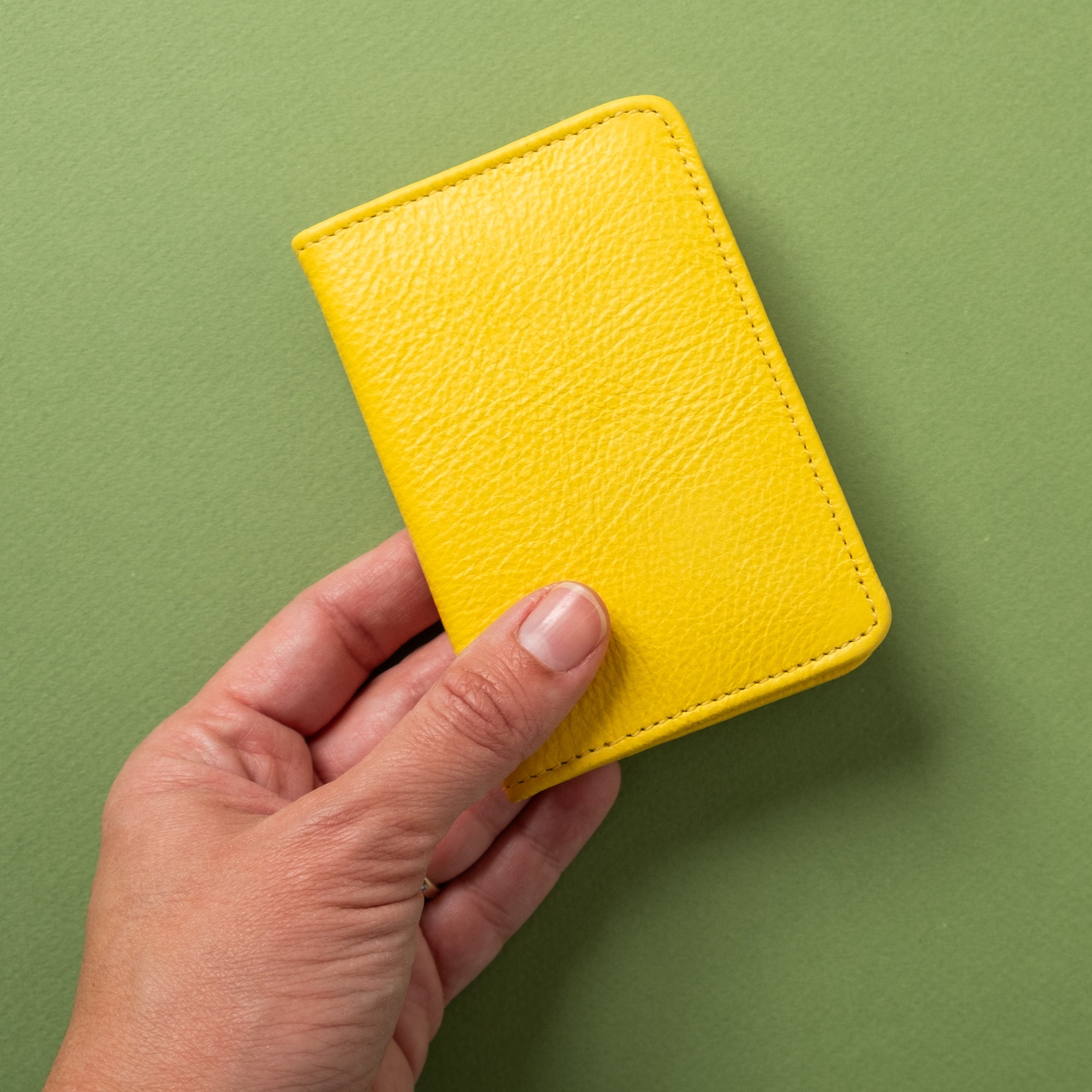 Hand holding a yellow leather wallet against a green background