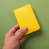 Hand holding a yellow leather wallet against a green background