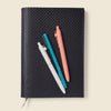 Black woven notebook with three pens on a beige background