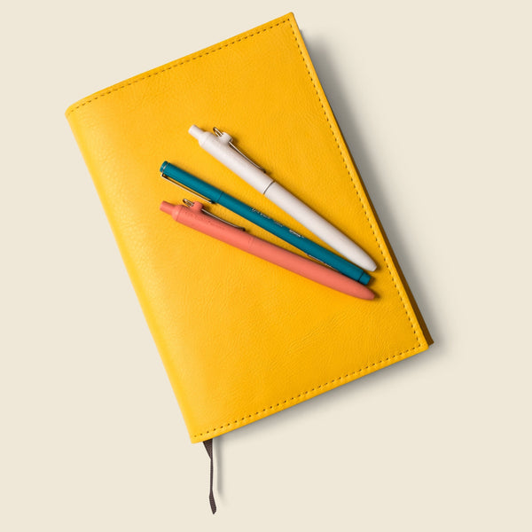 Yellow notebook with colorful pens on a beige background