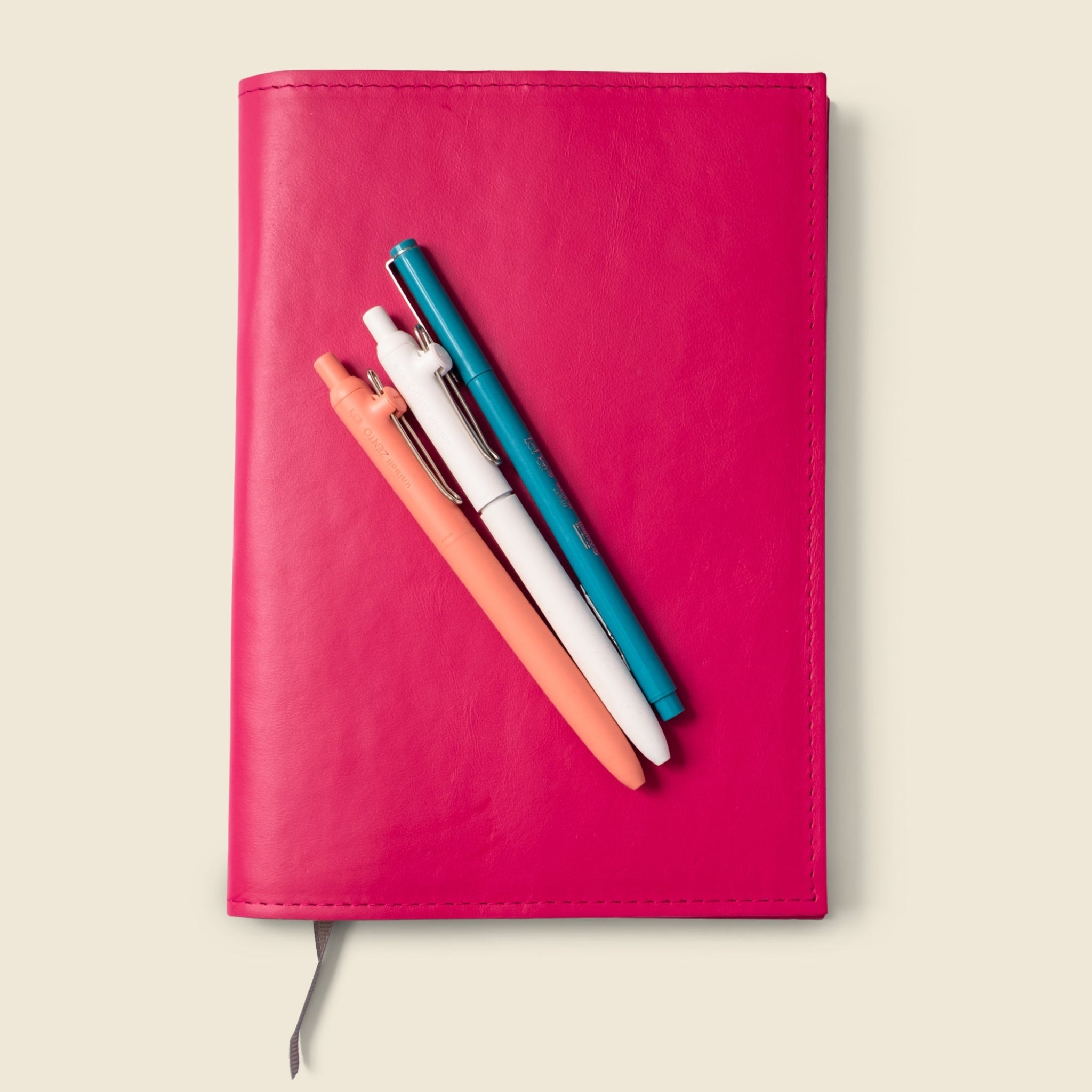 Pink notebook with colorful pens on a beige background
