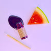 Small bottle with label, watermelon slice, and straw on a light purple background