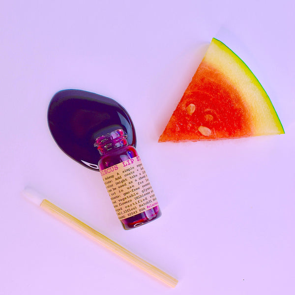 Small bottle with label, watermelon slice, and straw on a light purple background