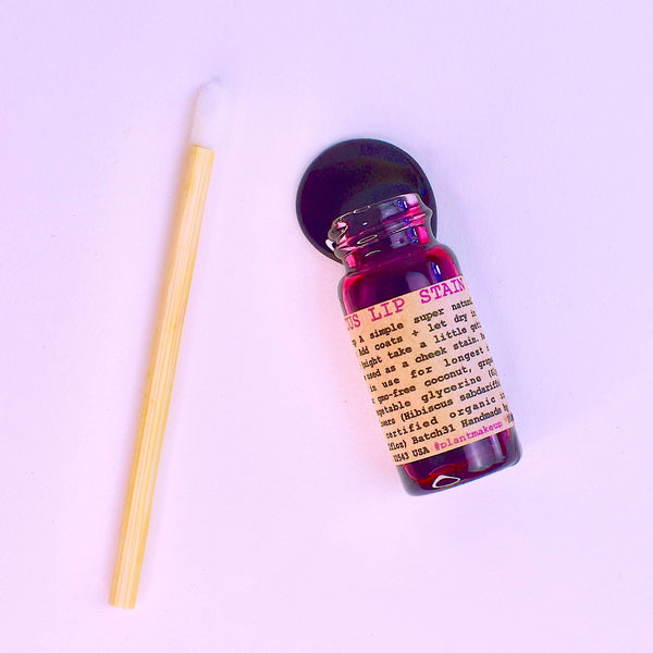 Small bottle with a wooden applicator on a light purple background