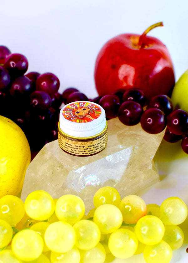 Jar of cream surrounded by fruits including grapes, an apple, and lemons on a white background