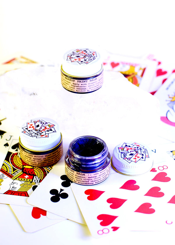 Three small containers with colorful labels on a white background with playing card designs.