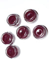 Set of six small containers with a dark red substance on a white background