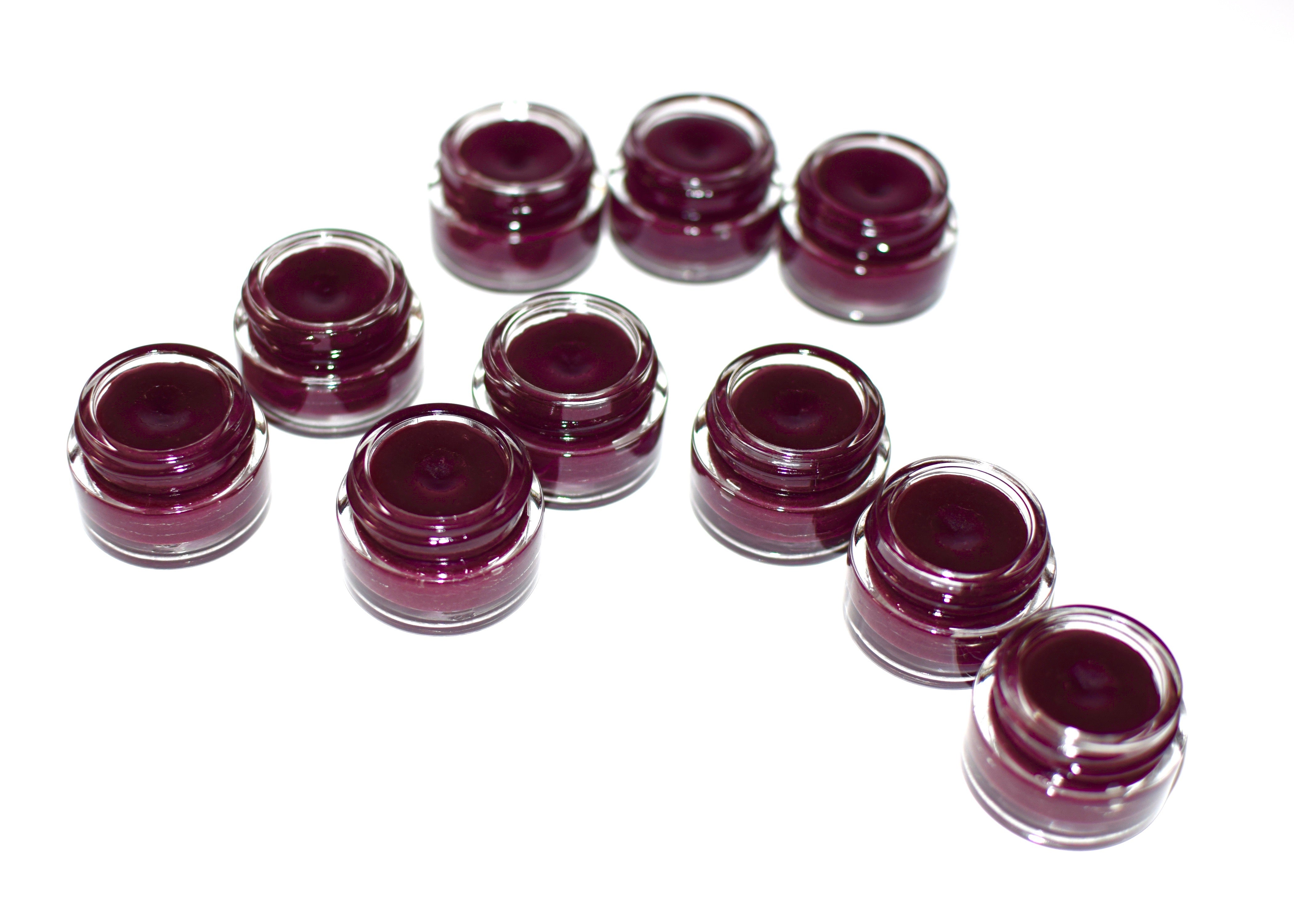Multiple small containers of dark purple cream or gel arranged in a circular pattern on a white background.