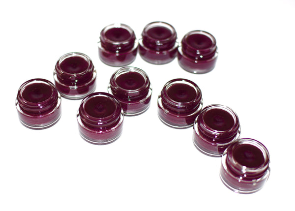 Multiple small containers of dark purple cream or gel arranged in a circular pattern on a white background.