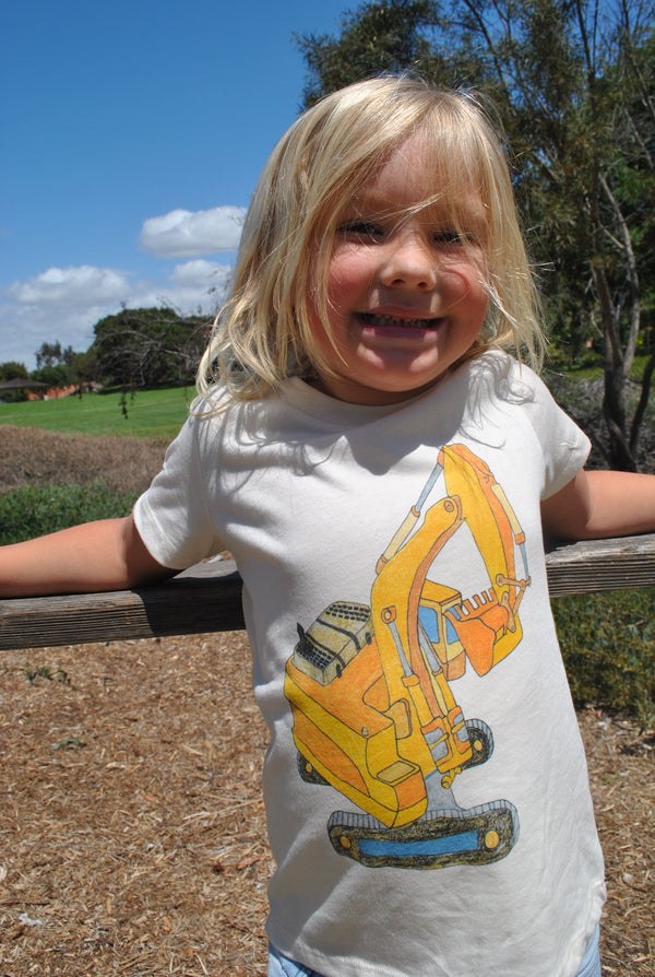 Child wearing a white t-shirt with a yellow excavator graphic outdoors.