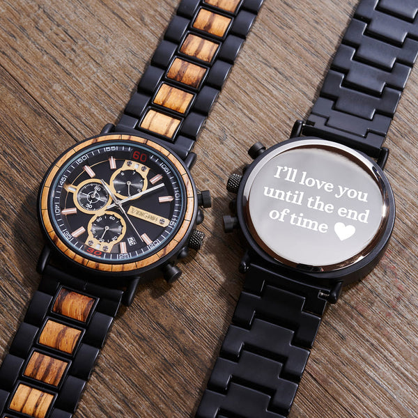 Two watches on a wooden surface, one with a wooden strap and detailed face, the other with a black strap and engraved message.