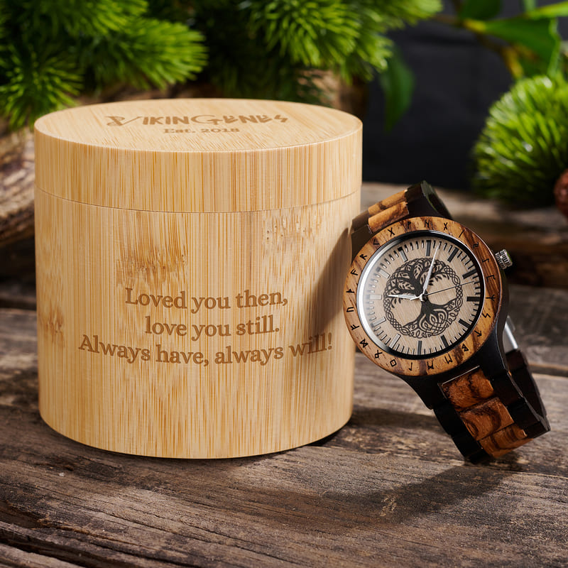 Wooden watch with engraved text on a wooden box, set against a natural background.