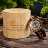 Wooden watch with engraved text on a wooden box, set against a natural background.
