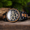 Close-up of black and gold wooden watch face showing multi-dial chronograph and date display