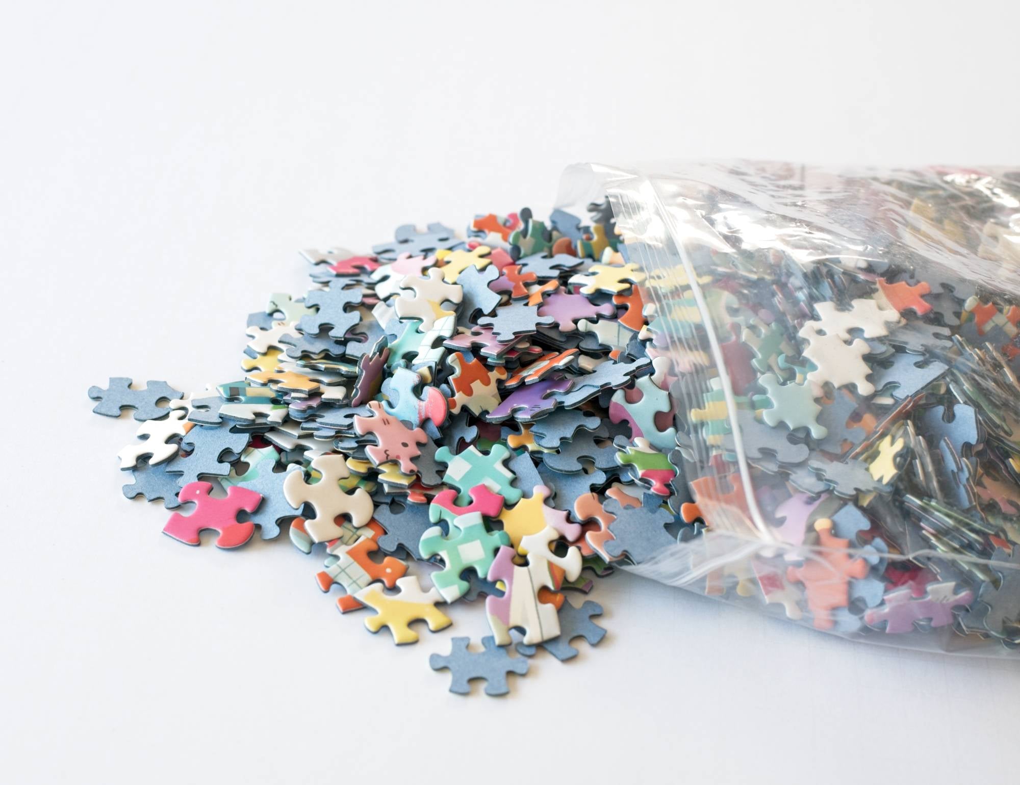 Colorful puzzle pieces spilling out of a clear plastic bag on a white background