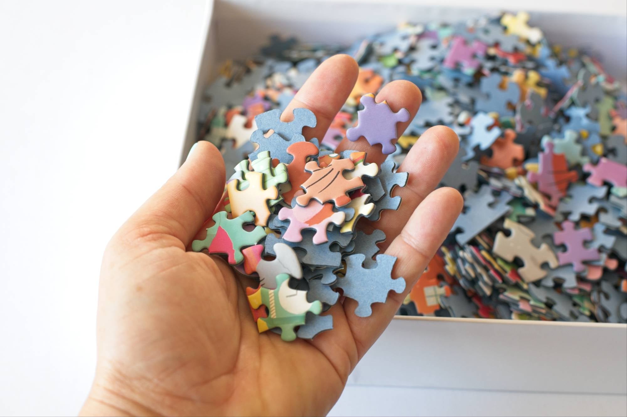 Hand holding colorful puzzle pieces with a box of puzzle pieces in the background