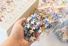 Birthday Suits puzzle pieces in reusable resealable bag alongside the giftable art box