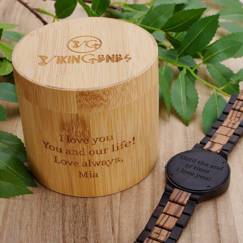 Wooden container with engraved message and a wooden watch on a wooden surface with leaves.