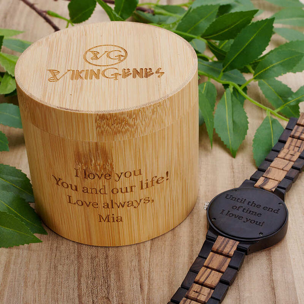 Wooden container with engraved message and a wooden watch on a wooden surface with leaves.