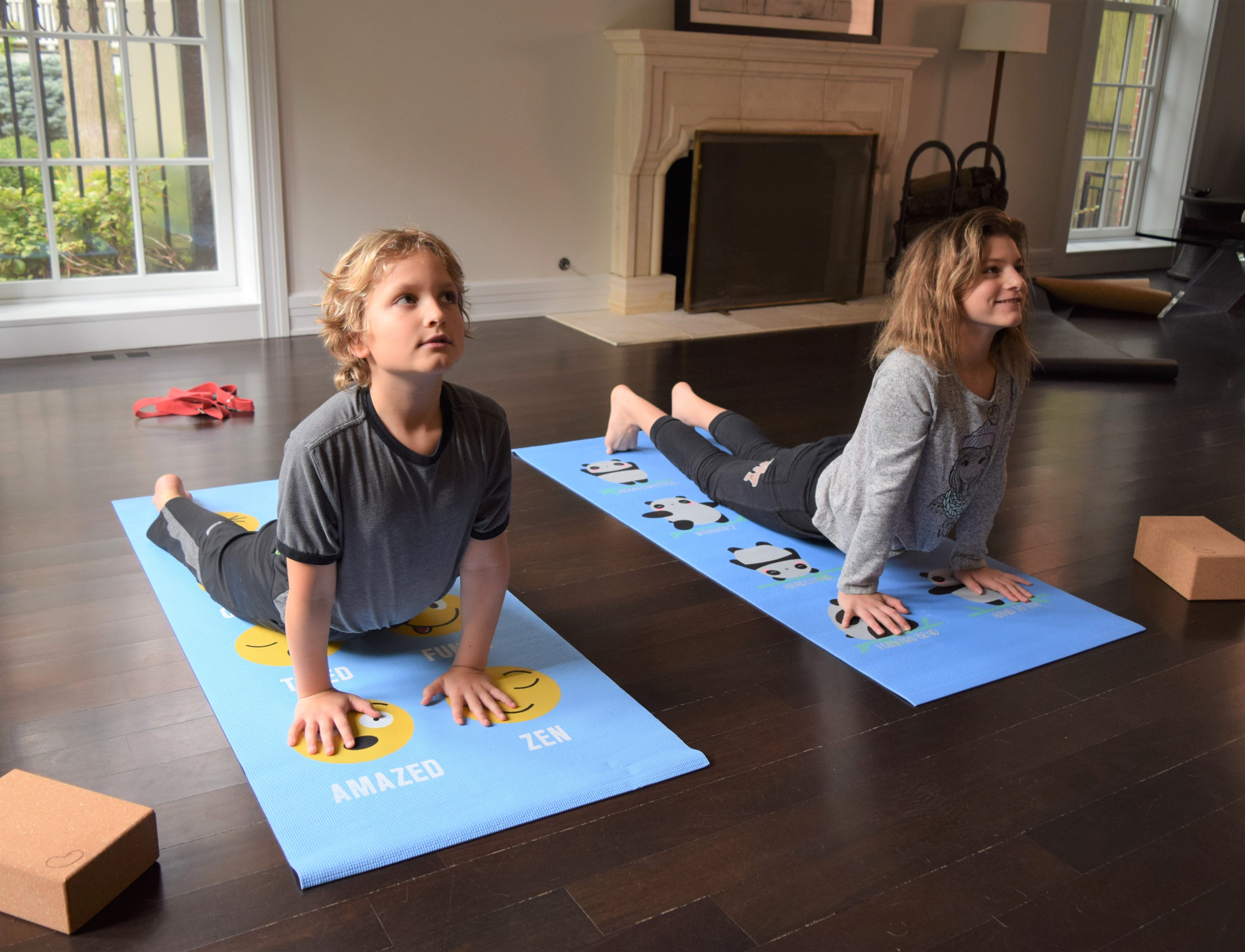 Two children on yoga mats with smiley face designs in a living room.