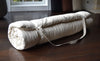 Rolled-up mattress on a wooden floor with a window in the background