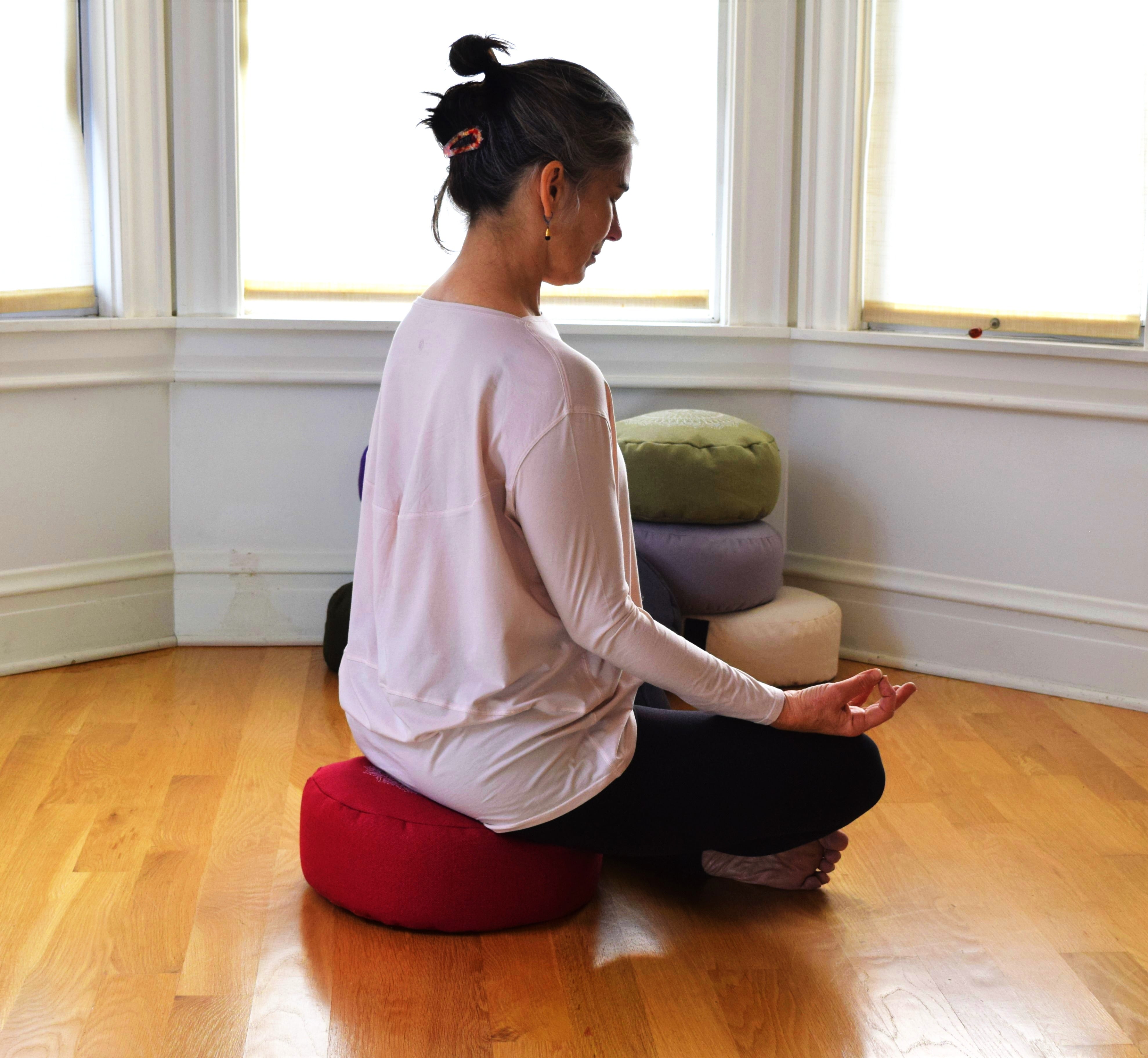 Woman meditating on a red zafu cushion — organic buckwheat yoga pillow by Bean Products