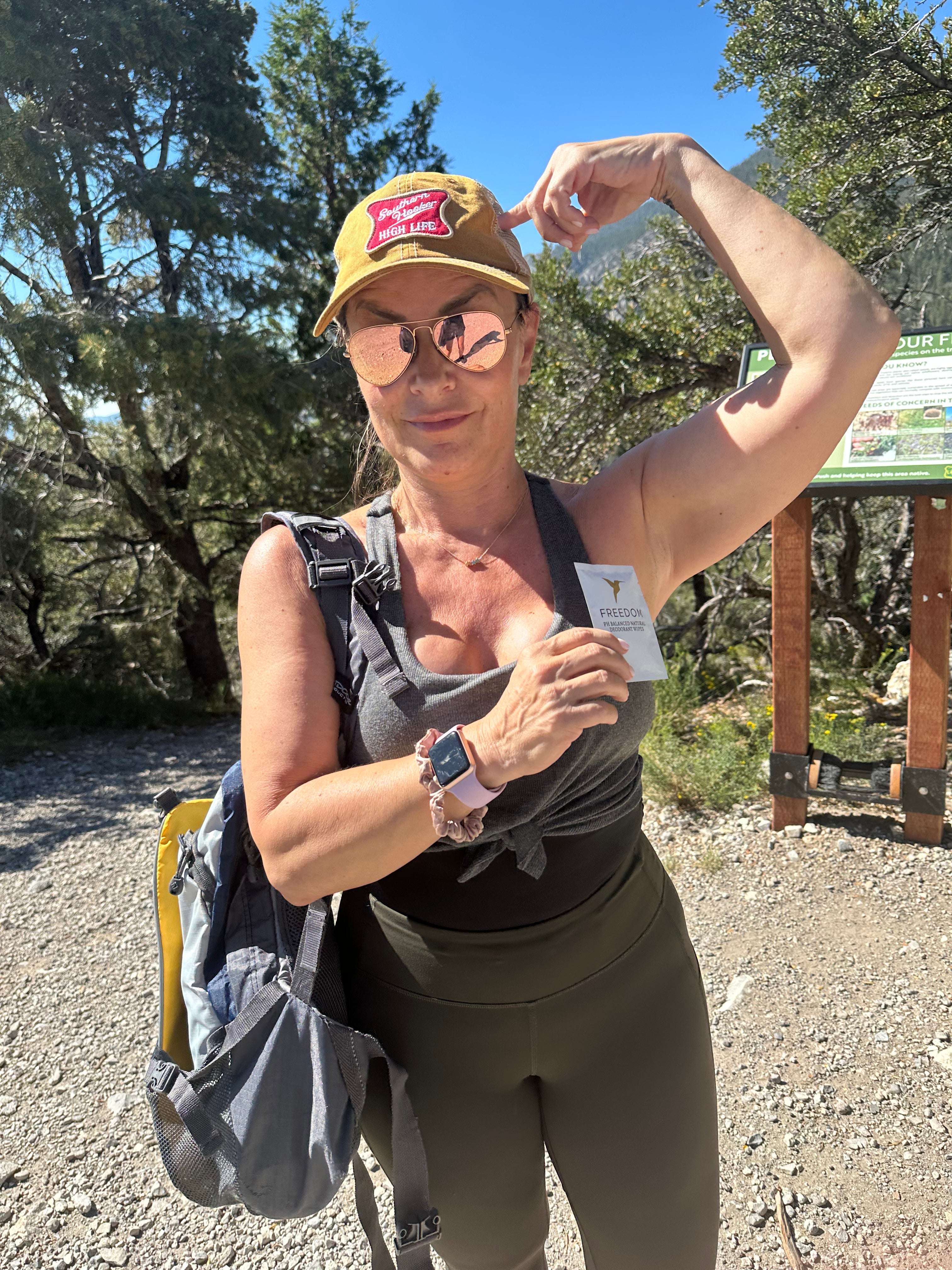 Woman hiking outdoors, wearing a cap and sunglasses, with a backpack and water bottle.