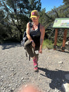 Woman hiking on a trail with a backpack and sunglasses, standing next to a informational sign.