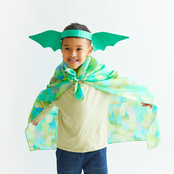 Child wearing a green superhero costume with cape and wings on a white background