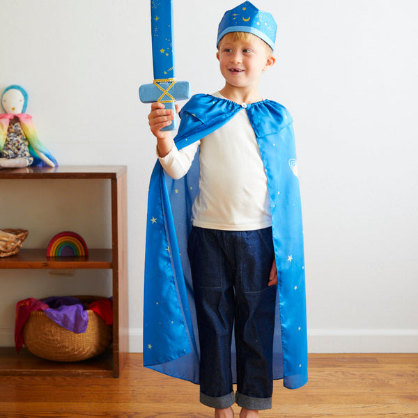Child in a blue superhero costume holding a toy sword in a room with a shelf in the background.