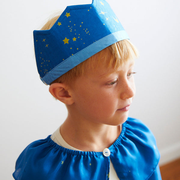 Child wearing a blue crown with star patterns on a plain background