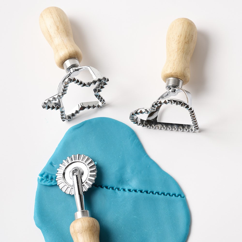 Three dough cutters with wooden handles on a white background, one cutting blue dough.