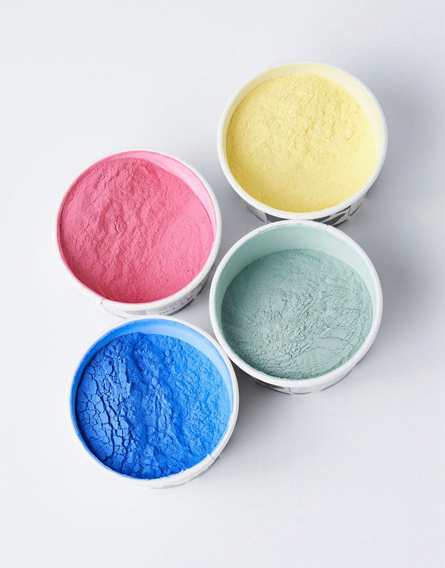 Four bowls with pink, yellow, blue, and green powders on a light gray background