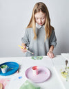 Young girl painting a ceramic item at a table with various art supplies.