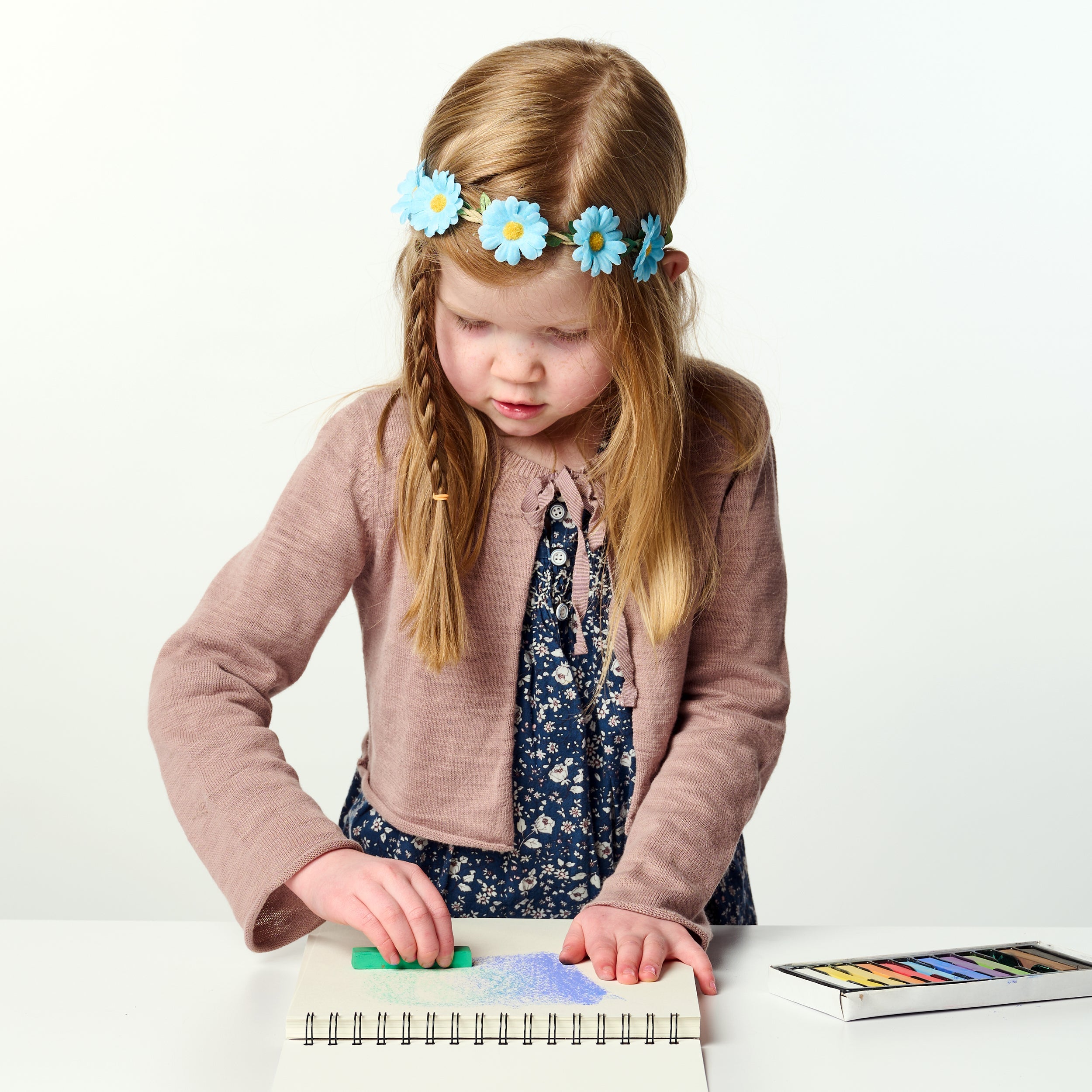 Young girl with a flower headband playing with colorful toys on a white background