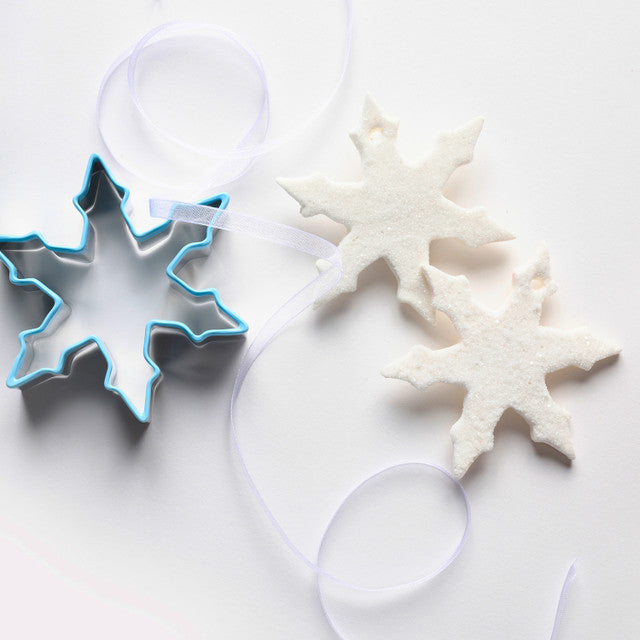 Snowflake-shaped cookie cutter with snowflake cookies on a white background