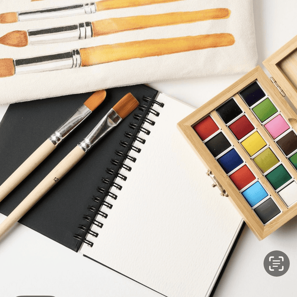 Watercolor travel bundle contents laid out including bamboo watercolor case, brushes, and watercolor pad